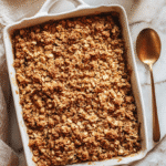 Homemade Apple Crisp top-down view with portion missing in white baking dish