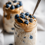 Top-down view of Protein Overnight Oats in a glass jar with almond butter and blueberries