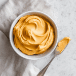 Top-down view of Pumpkin Cream Cheese Frosting in a bowl on marble countertop